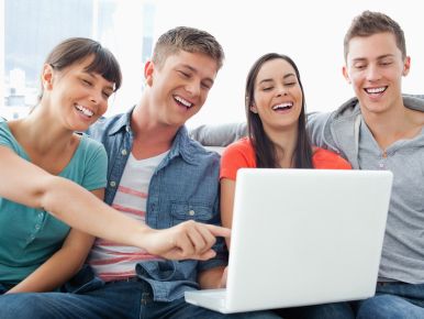 group of people laughing while gathered around a computer monitor