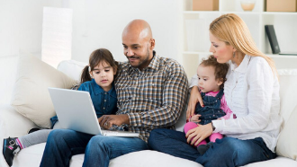 Picture of a man, woman and two children sitting on a couch looking at a laptop