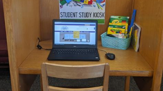 picture of a desk with a computer and a basket of school supplies on it
