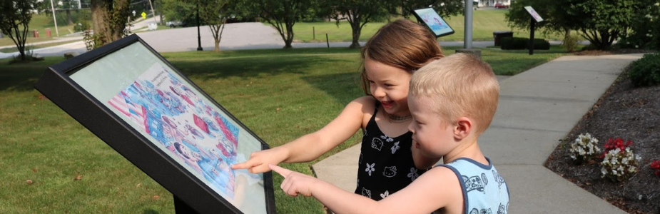 a preschool aged boy and girl reading a story board, pointing to a picture and smiling